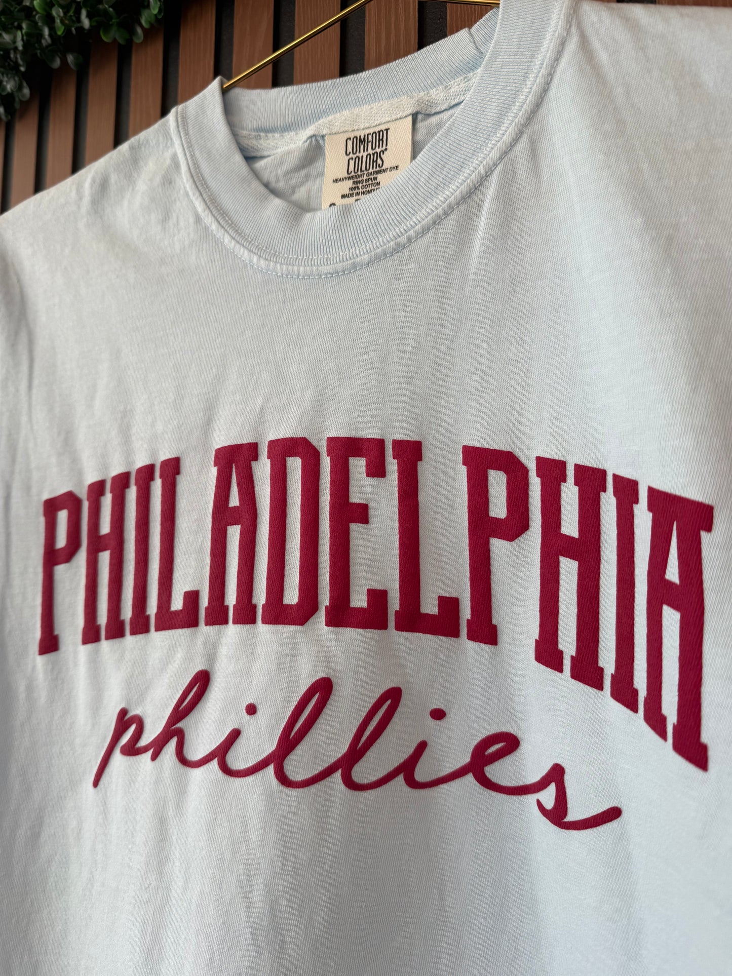 White t-shirt with red 'Philadelphia Phillies' text on a wooden surface