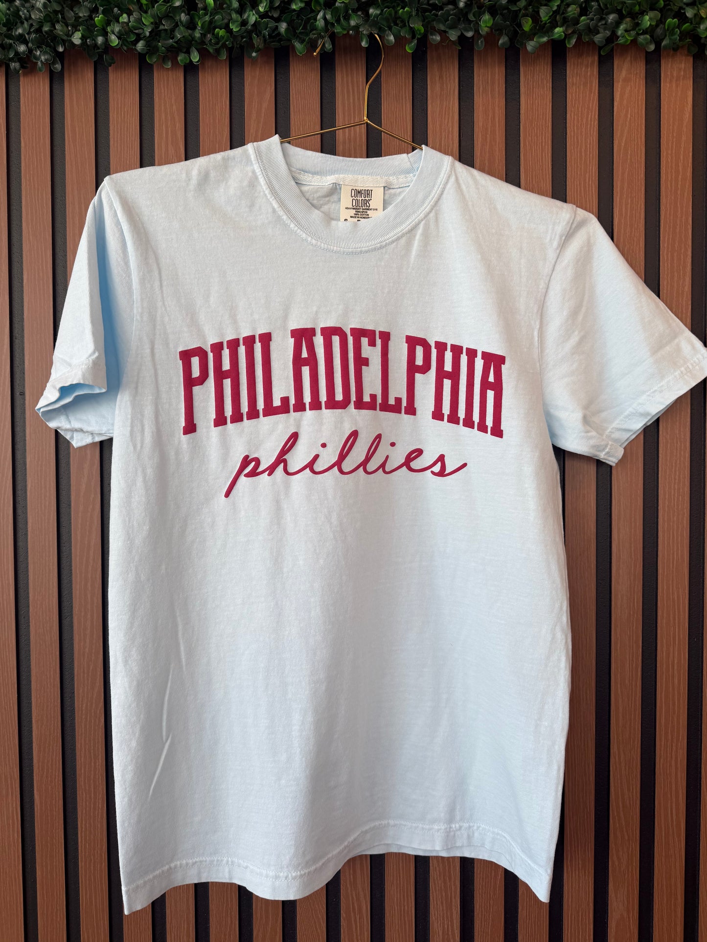 White t-shirt with red 'Philadelphia Phillies' text on a wooden surface