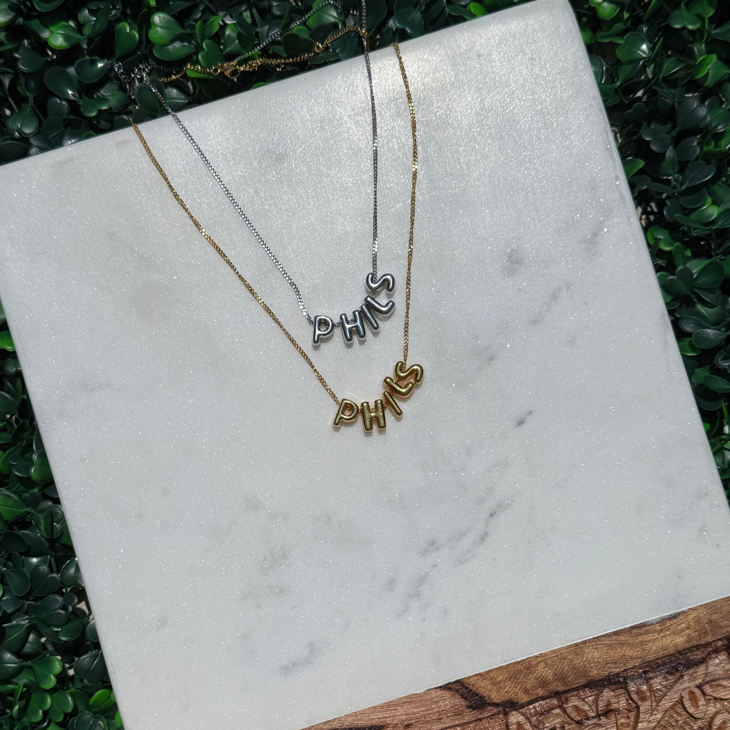 Two necklaces with 'PHILS' on a marble surface with a wooden base.