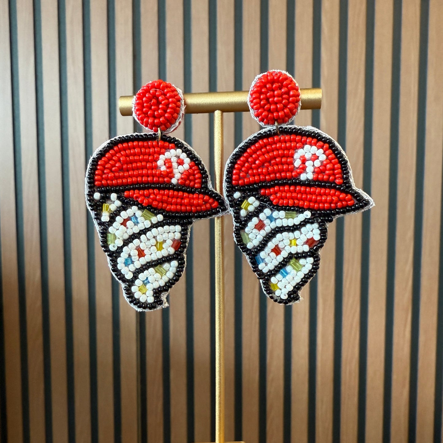 Pair of beaded earrings on a wooden stand with striped background
