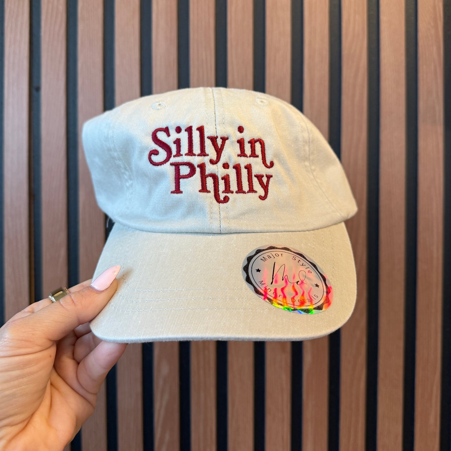 Beige cap with 'silly in Philly' text held against a wooden background