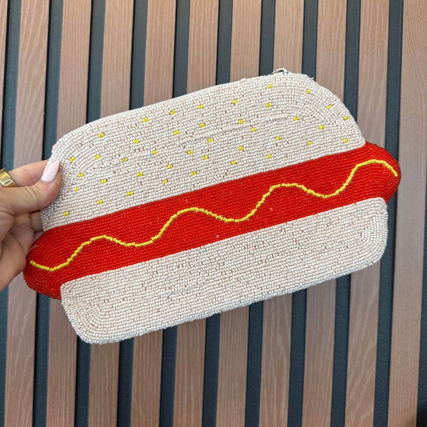 Hot dog-shaped pouch with red and yellow details held by a hand on a wooden surface