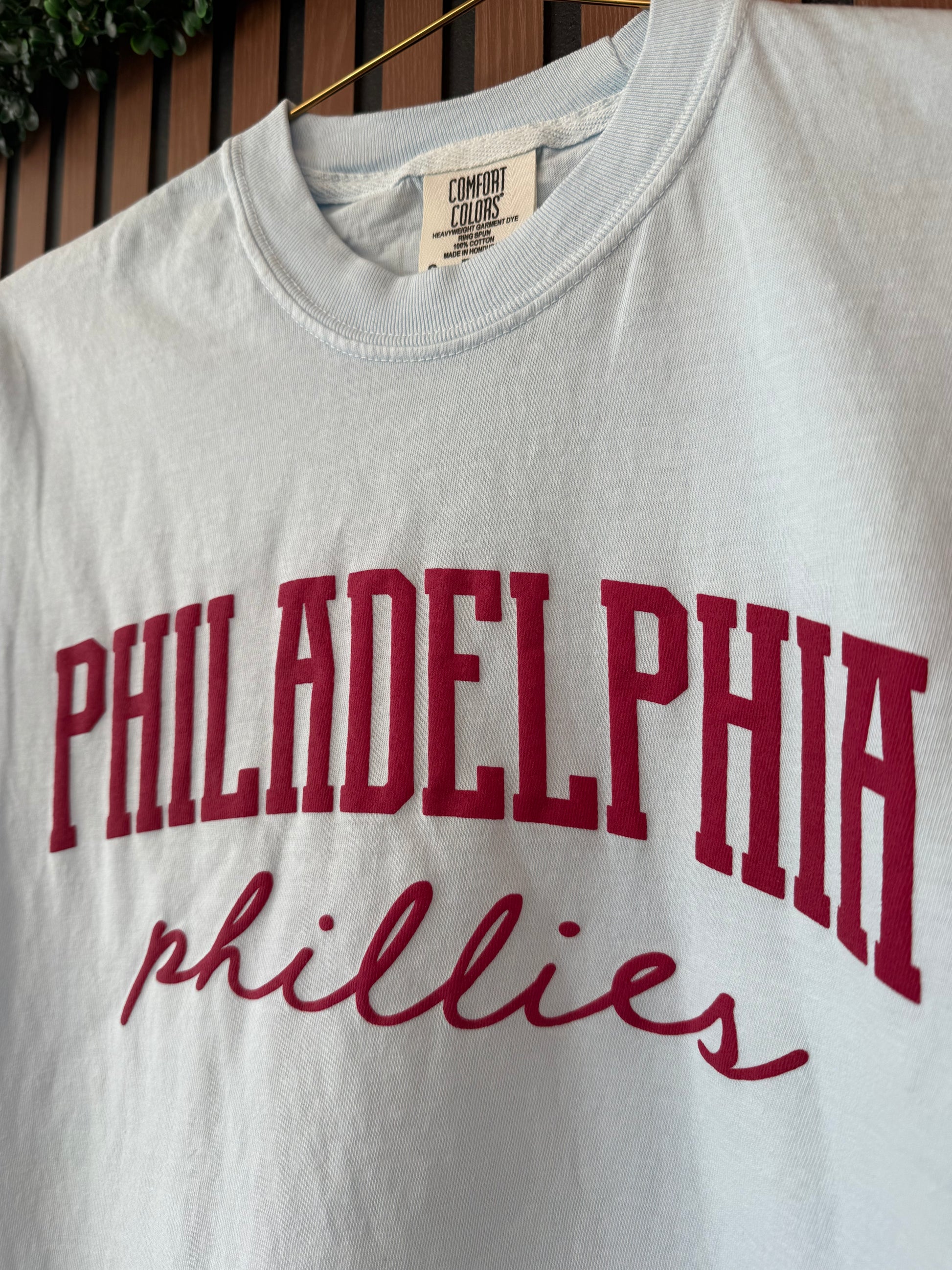 White t-shirt with red 'Philadelphia Phillies' text on a wooden surface