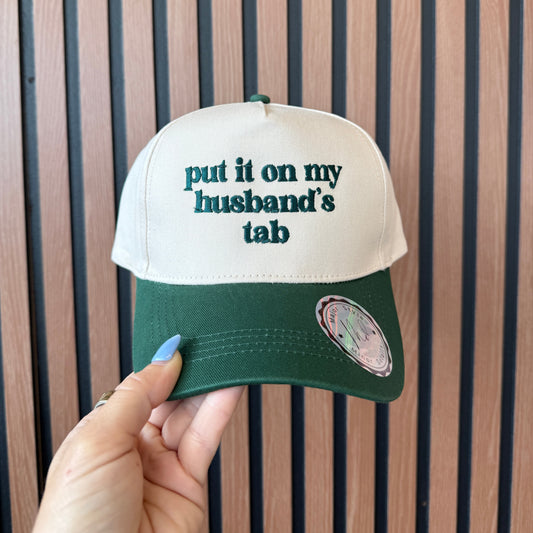 Green and beige cap with text held by a hand on a wooden surface