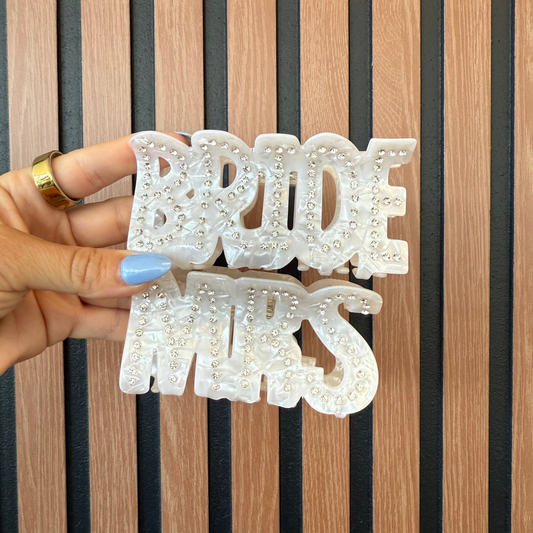 Hand holding a decorative claw clip with 'Bride & Mrs.' text against a striped background