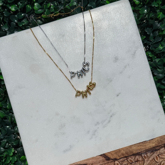 Two necklaces with 'PHILS'  on a marble surface with a wooden base.