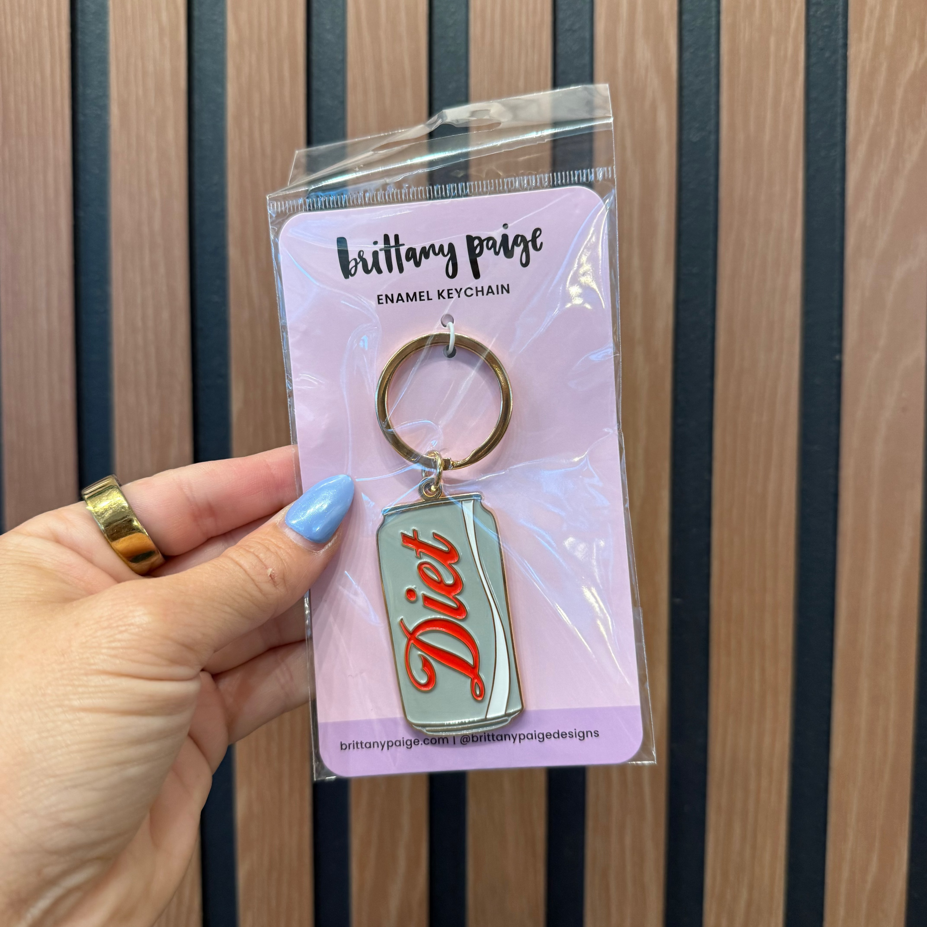 Hand holding a keychain with 'Diet' text against a striped background