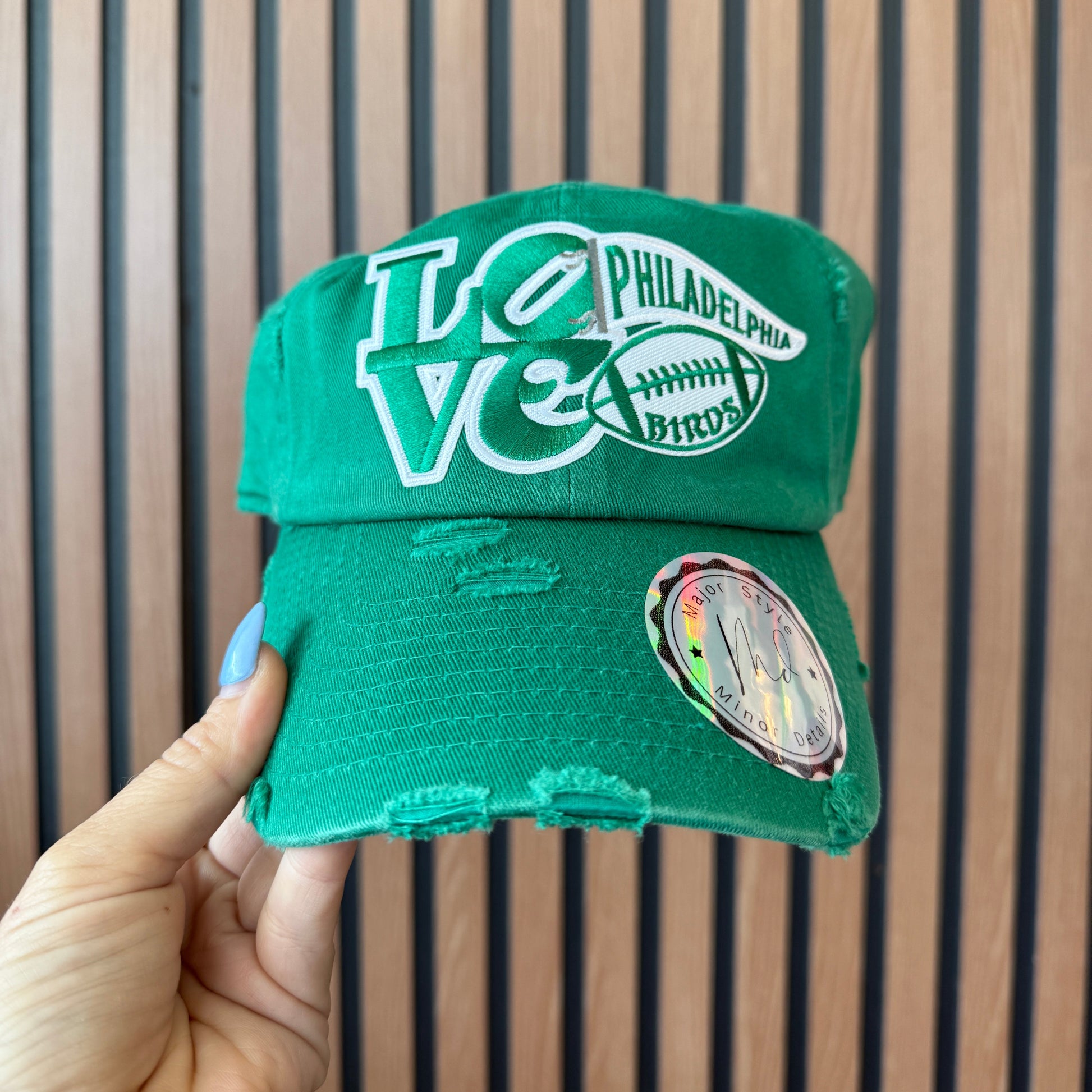 Green hat with 'Philadelphia' branding held by a hand against a striped background