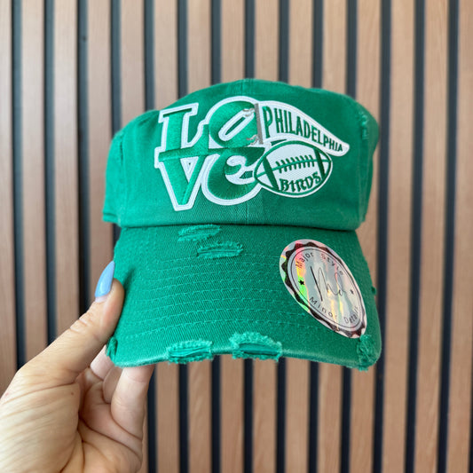 Green hat with 'Philadelphia' branding held by a hand against a striped background