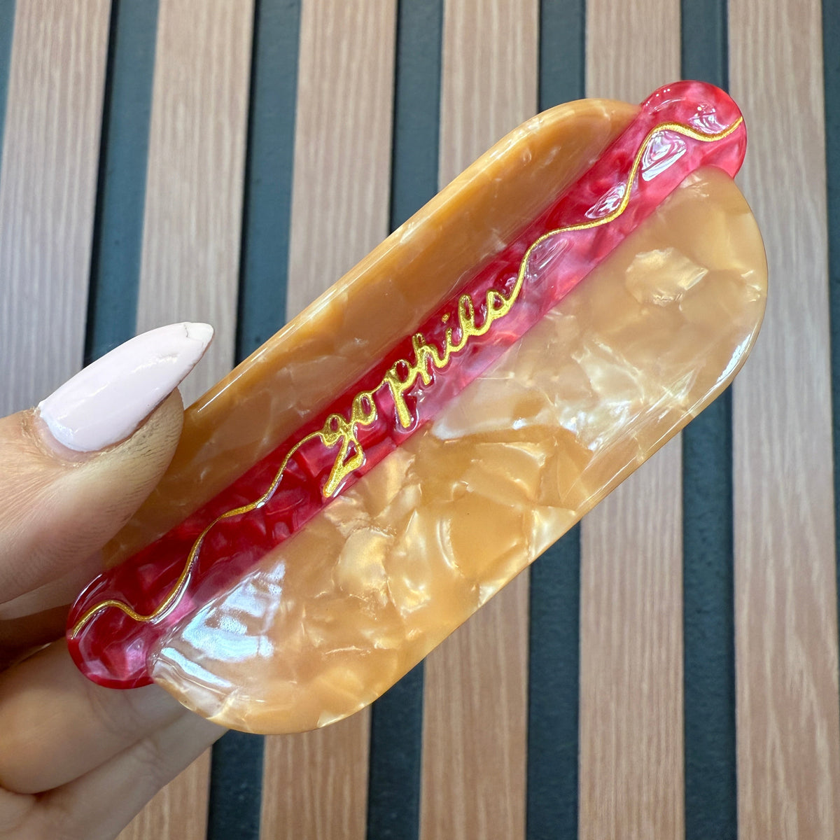 Hot dog with a bun held by a hand on a striped background