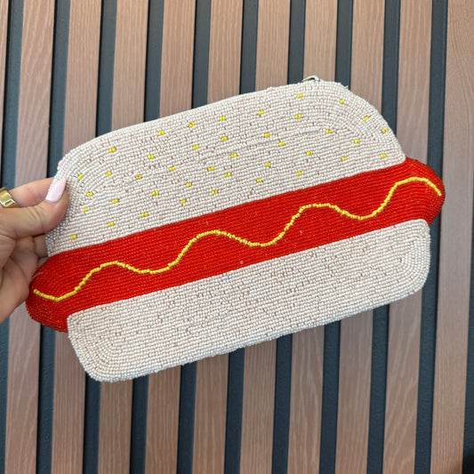 Hot dog-shaped pouch with red and yellow details held by a hand on a wooden surface