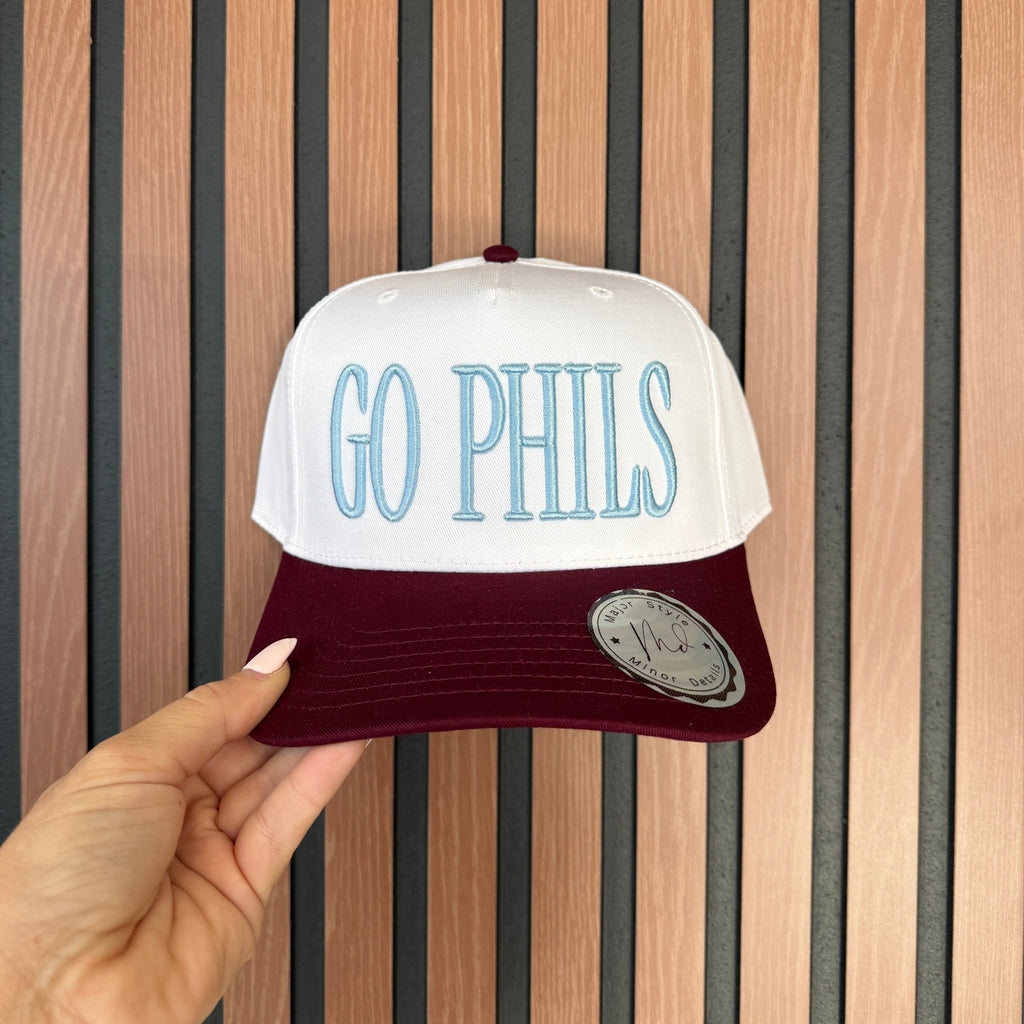 Cap with 'GO PHILS' text held by a hand on a wooden slat background
