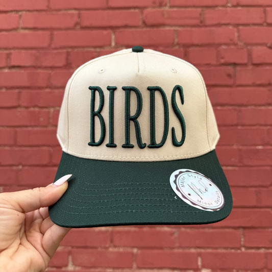 Cap with 'BIRDS' text held against a brick wall