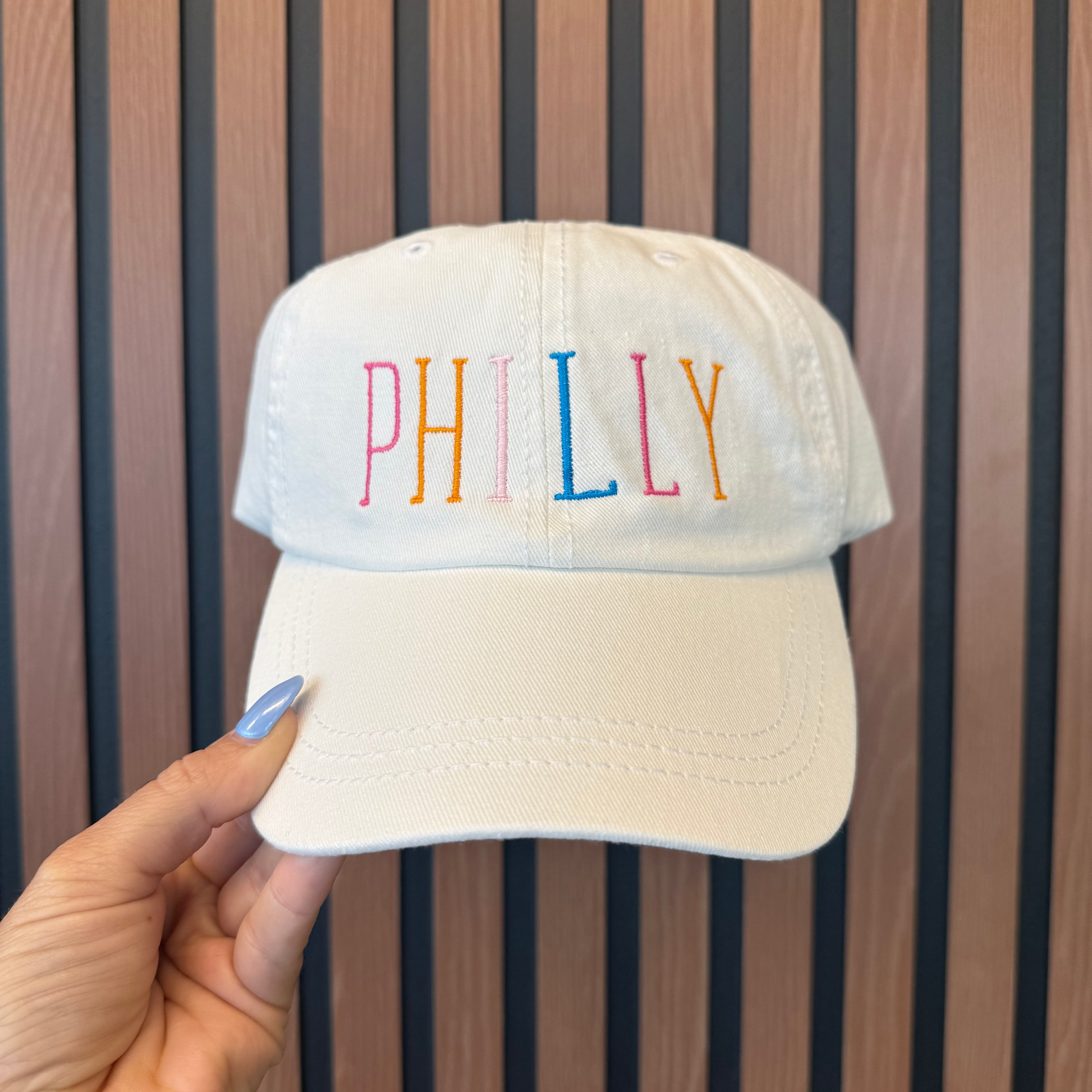 White cap with 'PHILLY' in colorful letters held against a striped background