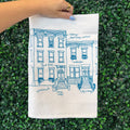 Hand holding a tea towel with architectural design on a green grass background