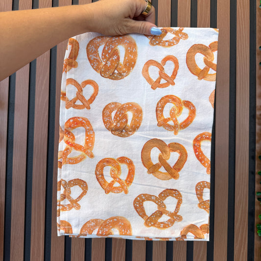 Hand holding a towel with pretzel pattern on a wooden surface