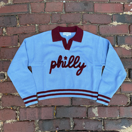 Light blue sweater with 'philly' text on a brick wall background
