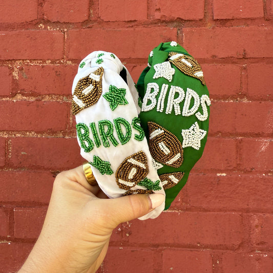 Green and white headbands with 'BIRDS' text held against a red brick wall.